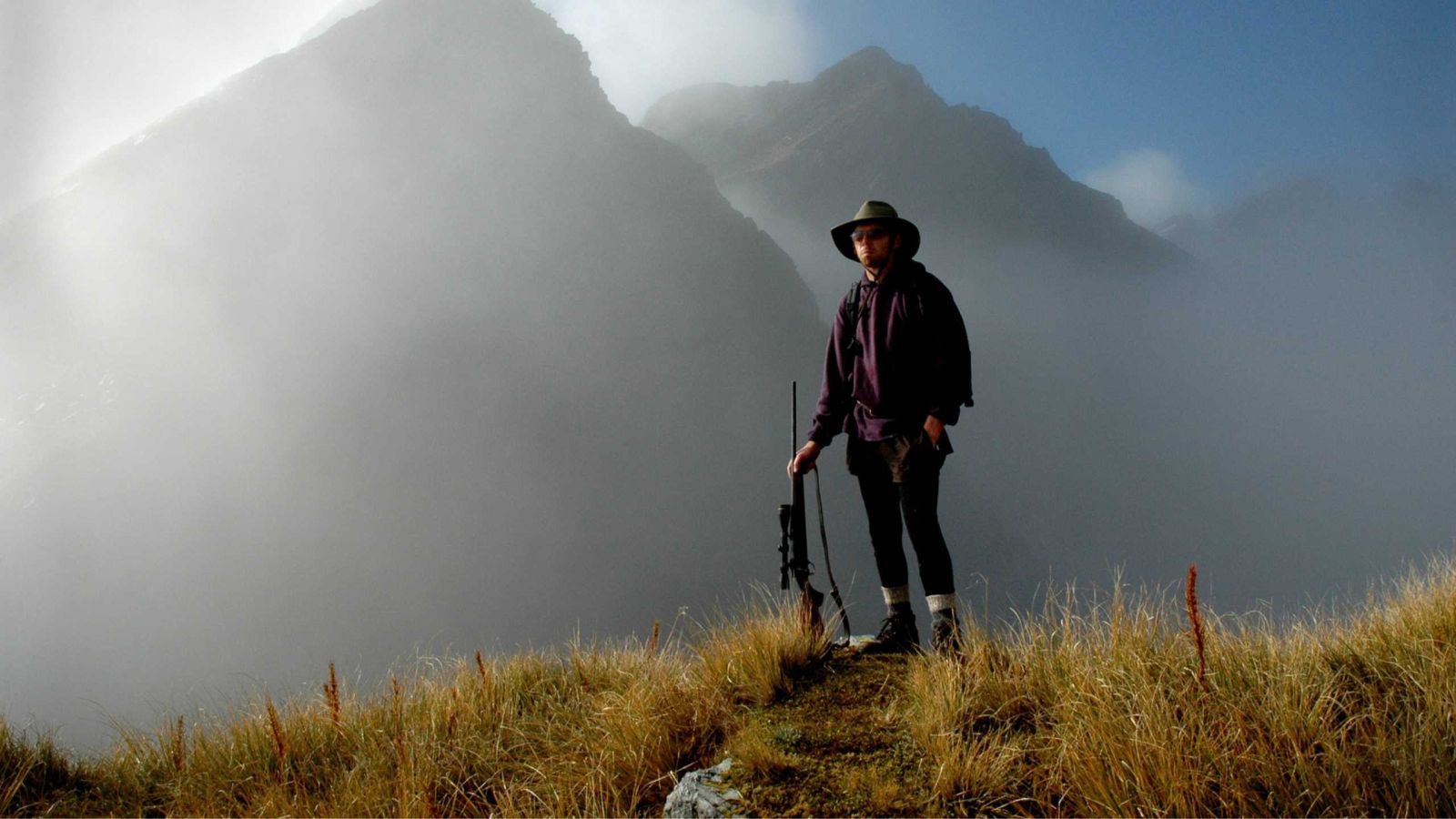 hunter on top of hill with mountains in behind